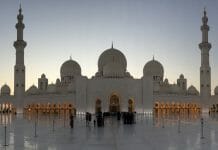 a large white building with domes and people standing in front of it with Sheikh Zayed Mosque in the background