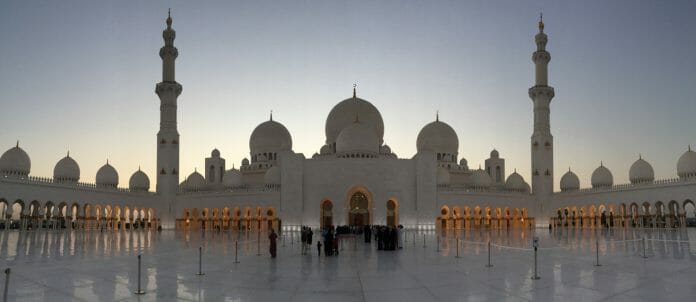 a large white building with domes and people standing in front of it with Sheikh Zayed Mosque in the background