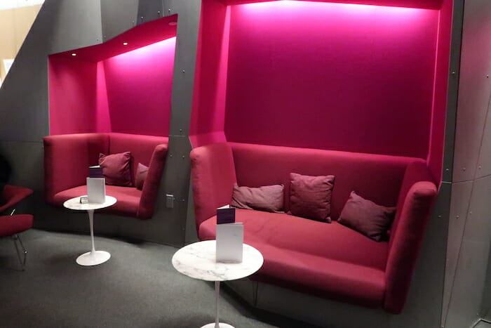 a red couches with pillows and a table with a pink wall behind them