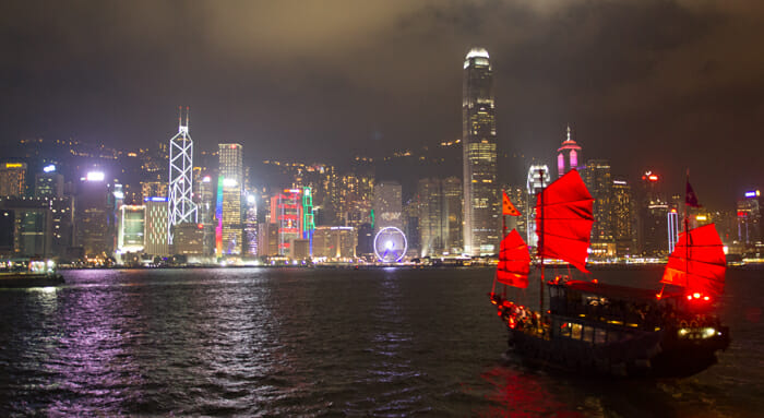 a boat with red sails in the water with a city in the background