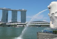 a water spraying out of a body of water with Marina Bay Sands in the background