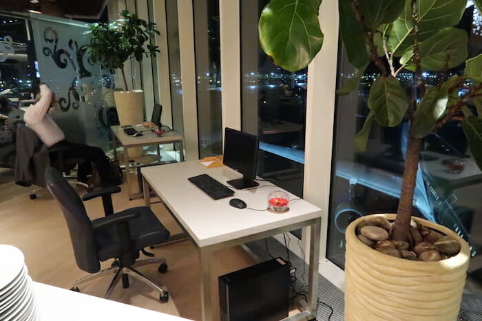 a desk with a computer and chairs in front of a window