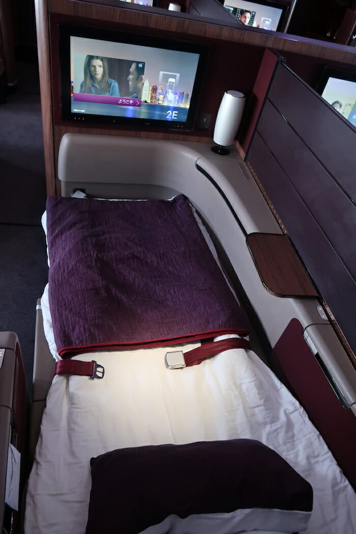 a bed with a blanket and a tv in the back of a seat