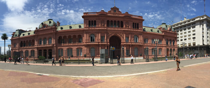 a large building with a gated entrance with Casa Rosada in the background