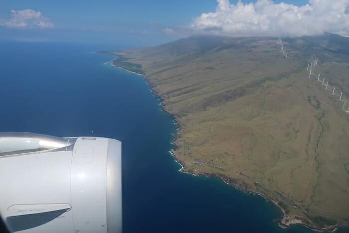 an airplane wing over a land with a body of water and a mountain