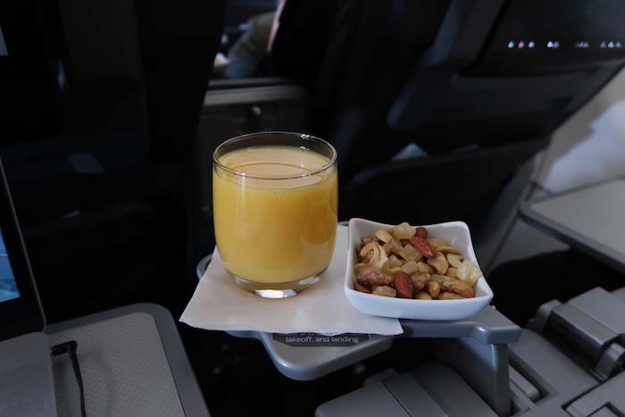 a glass of orange juice and a bowl of nuts on a tray