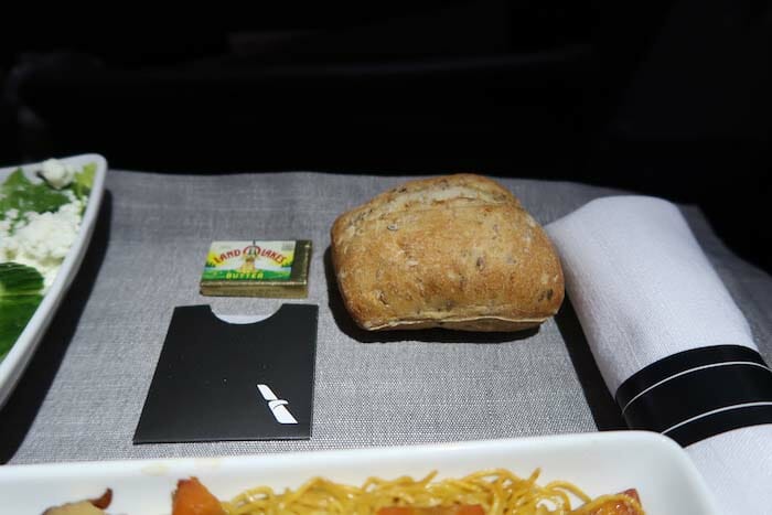 a piece of bread next to a plate of pasta and a packet of butter