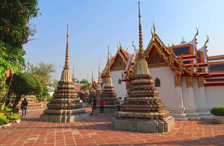 a group of pagodas in front of a white building with Wat Pho in the background