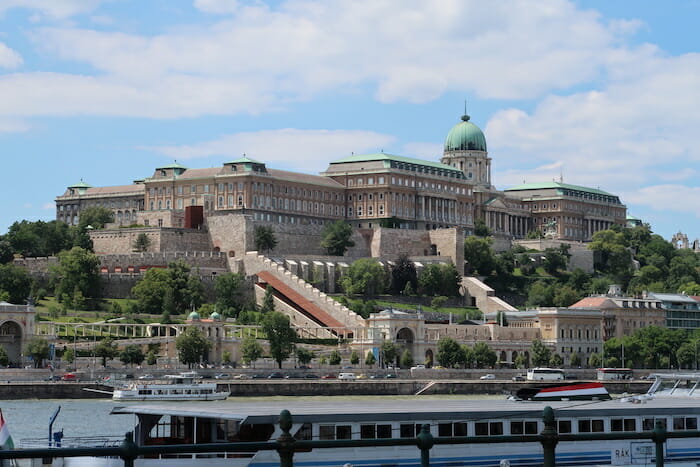 a large building with a green dome on top with Buda Castle in the background