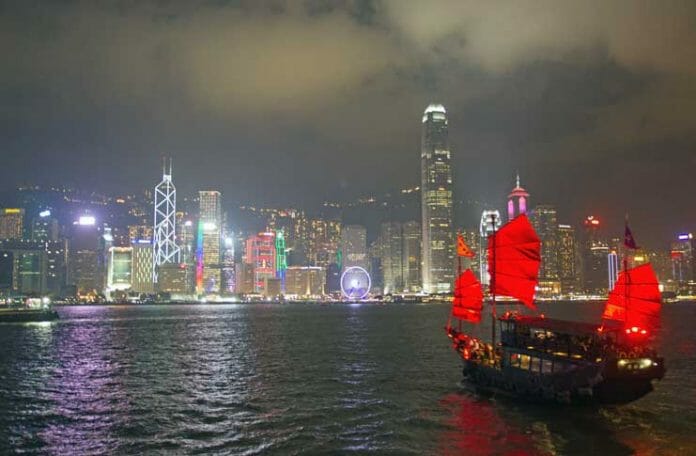 a boat with red sails in the water with Victoria Harbour in the background