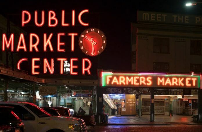 a neon sign at night with Pike Place Market in the background