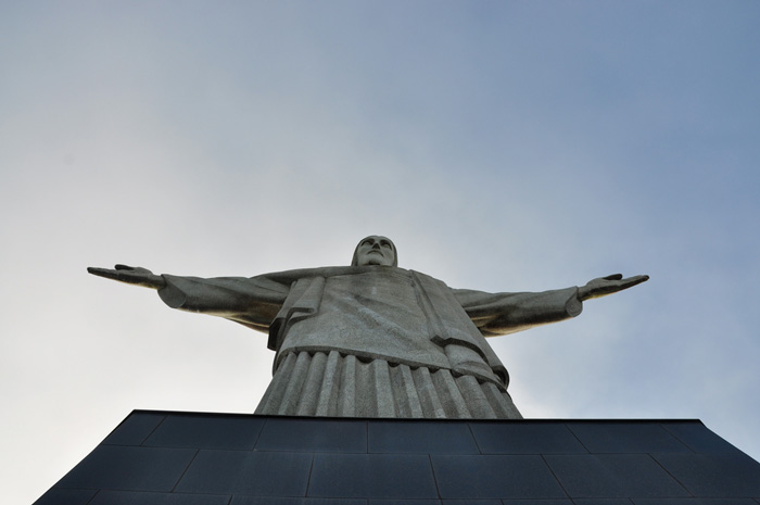 a statue of a man with arms out with Christ the Redeemer in the background