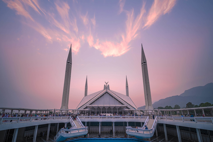 a large white building with towers with Faisal Mosque in the background