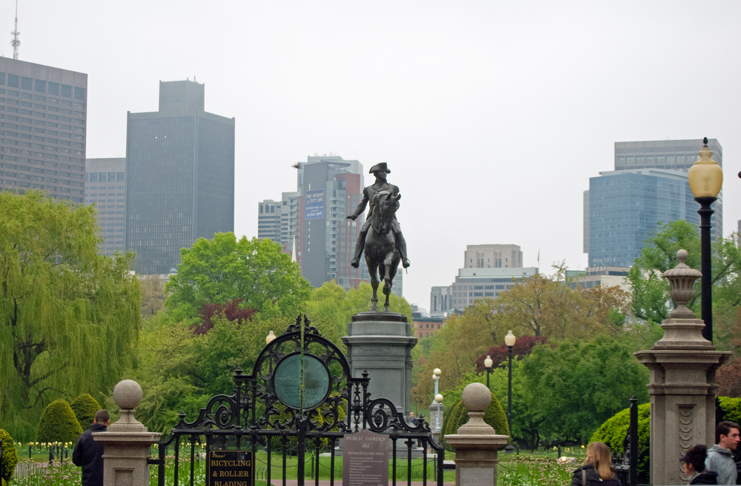 a statue of a man on a horse in a park with a city in the background