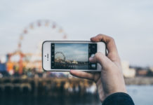 a hand holding a phone taking a picture of a ferris wheel