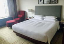 a bed with a white sheet and a red chair in a room