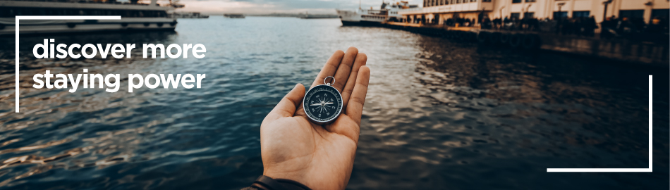 a hand holding a compass in front of a body of water