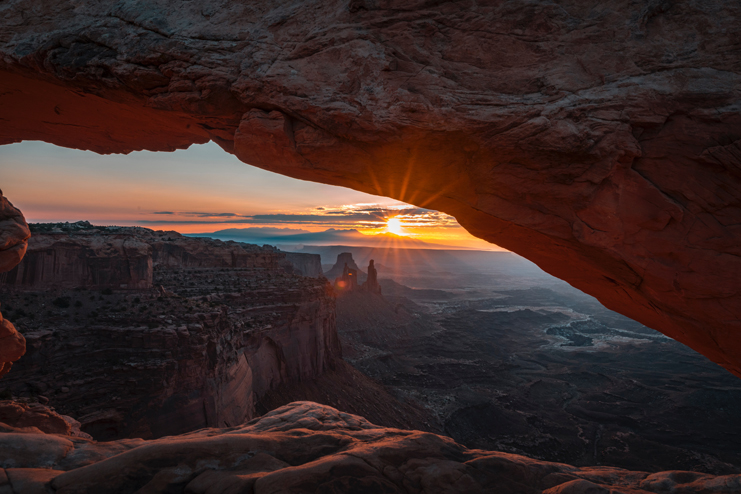 a sun shining through a rock arch