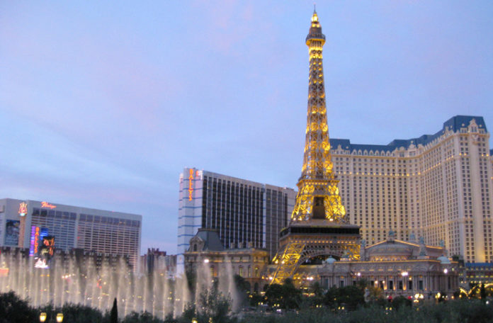 a large tower with lights in front of a fountain with Paris Las Vegas in the background