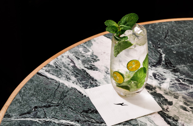 a glass of water with limes and mint leaves on a napkin on a table