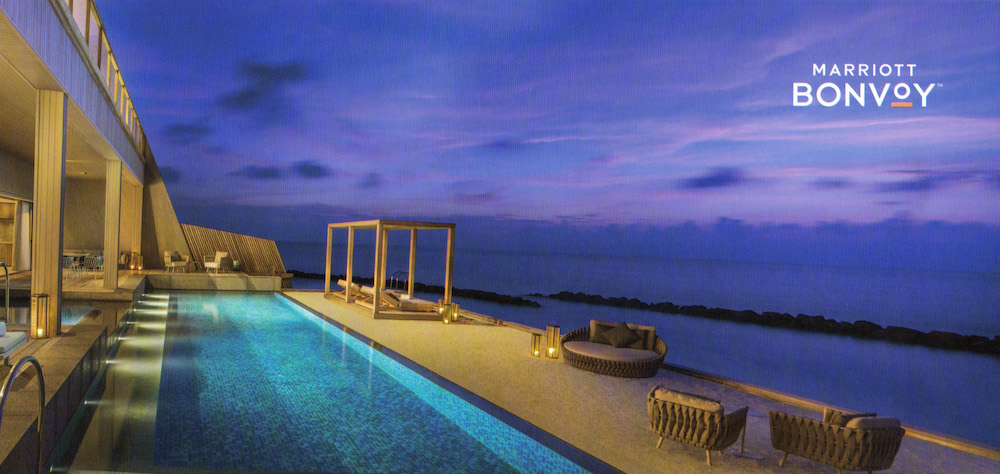 a pool with a deck chair and a lounge chair on a deck overlooking the ocean