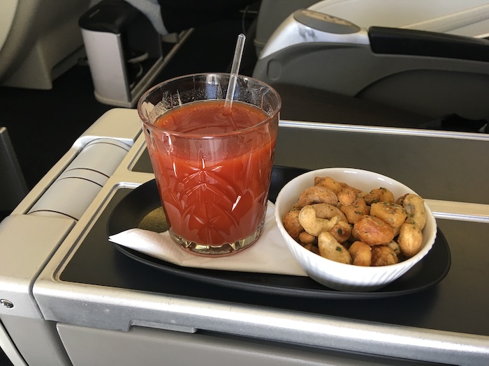 a glass of tomato juice and a bowl of nuts on a tray