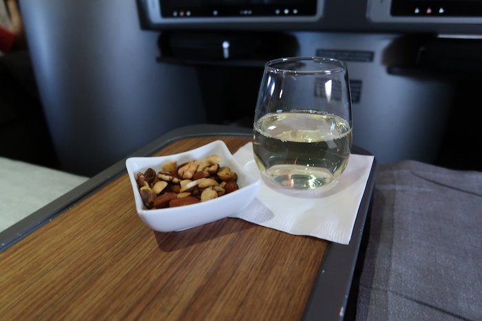 a glass of water and a bowl of nuts on a tray
