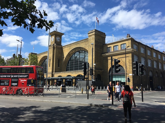 a large building with a clock tower and people walking around with London King's Cross railway station in the background