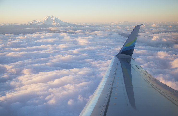 an airplane wing and clouds and a mountain