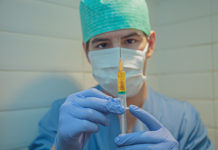a person wearing a mask and gloves holding a syringe
