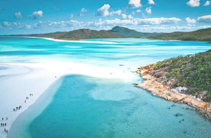 a beach with blue water and hills with Whitehaven Beach in the background