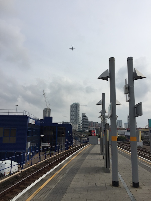 a train station with a plane flying in the sky