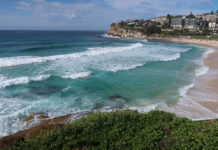 a beach with waves crashing on the shore with Bondi Beach in the background