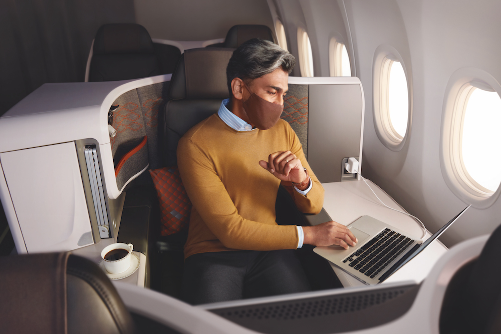 a man wearing a mask sitting in an airplane with a laptop