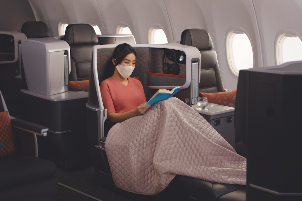 a woman in a mask reading a book on an airplane