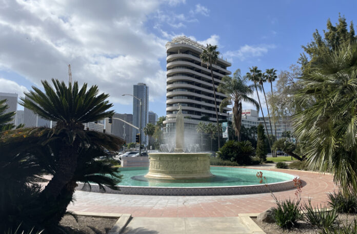 a fountain in a park with palm trees and buildings in the background