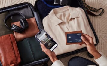 Review: The Hilton Honors American Express Aspire Card (175,000 bonus points & Diamond Elite status) a person holding a phone and a wallet next to luggage
