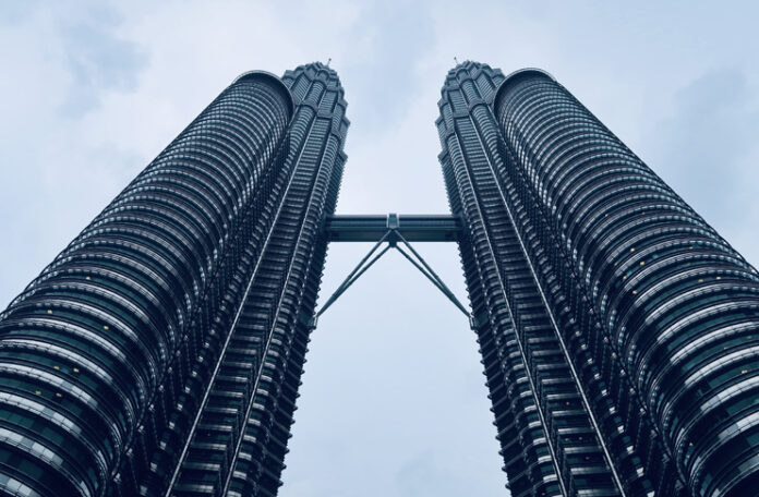 looking up view of two tall buildings with Petronas Towers in the background