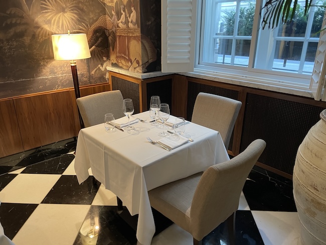 a table with a white tablecloth and chairs in a room with a lamp