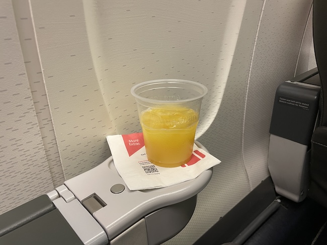 a cup of orange juice on a napkin on a seat