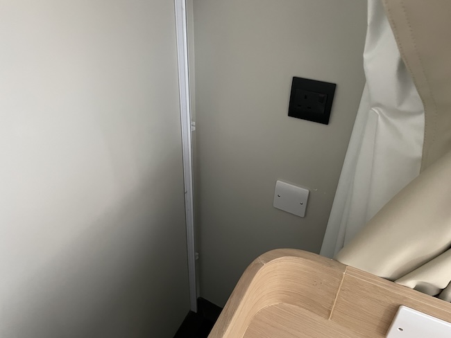 a white wall with a light switch and a wood shelf