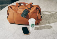 a brown bag with a black tag and a phone and a cup on a marble surface