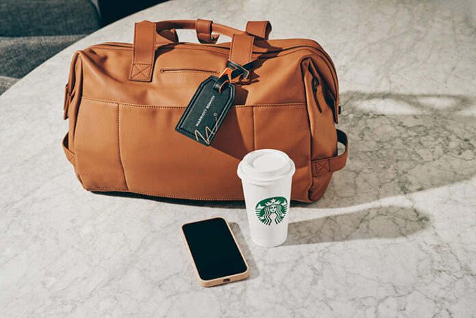 a brown bag with a black tag and a phone and a cup on a marble surface