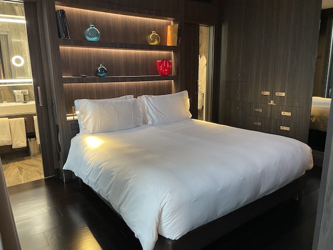 a bed with white sheets and a shelf with colorful vases